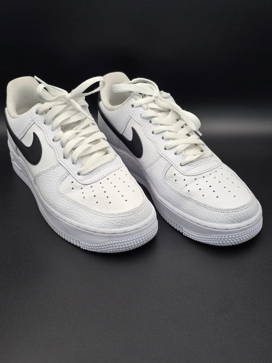 Weiße Sneaker mit schwarzem Swoosh, seitlich auf schwarzem Hintergrund fotografiert