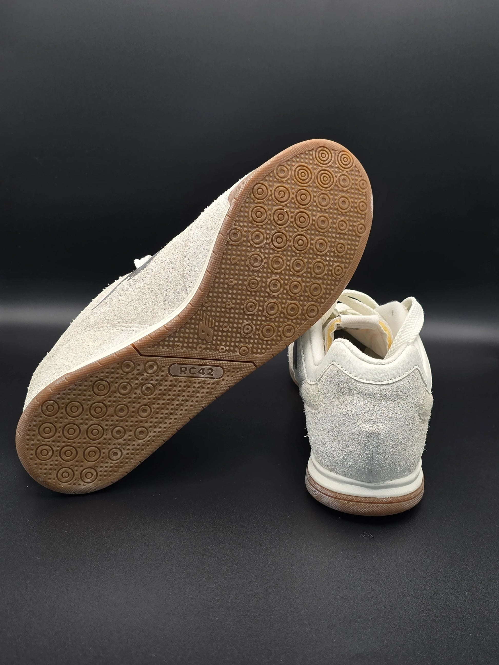 Weiße Sneaker mit Gummisohle und Wildleder-Details auf schwarzem Hintergrund, nachhaltige Mode