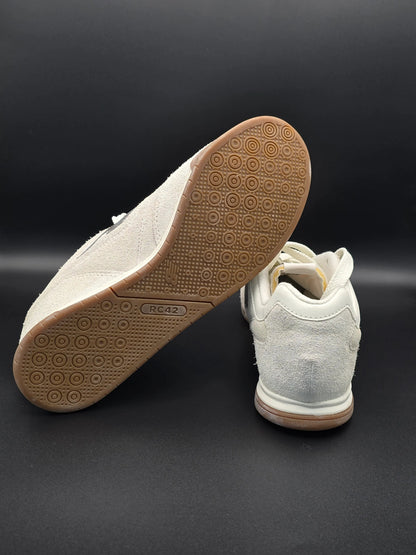 Weiße Sneaker mit Gummisohle und Wildleder-Details auf schwarzem Hintergrund, nachhaltige Mode