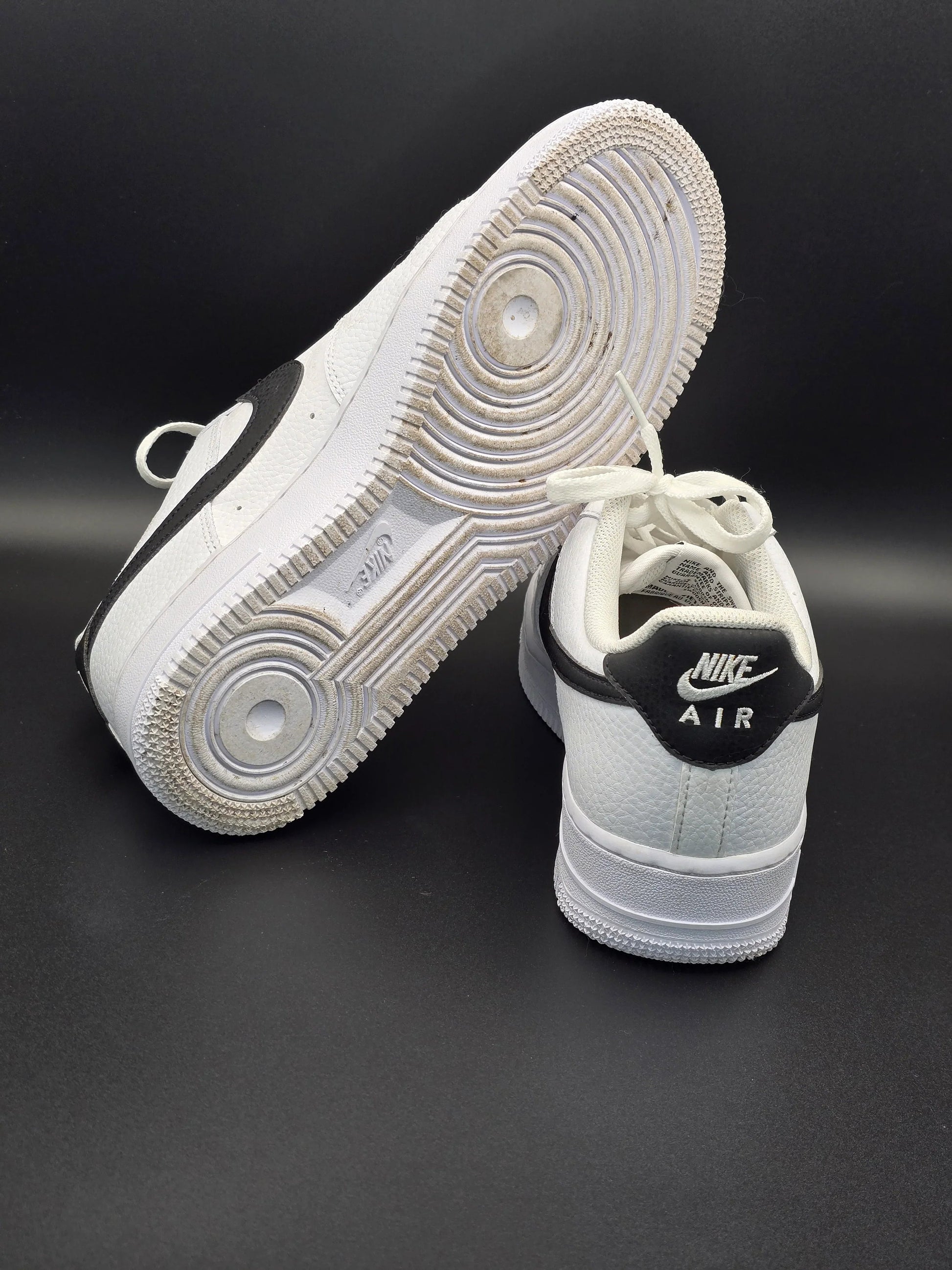 Weiße Sneaker mit schwarzem Nike-Logo auf schwarzem Hintergrund, trendy Sportschuhe