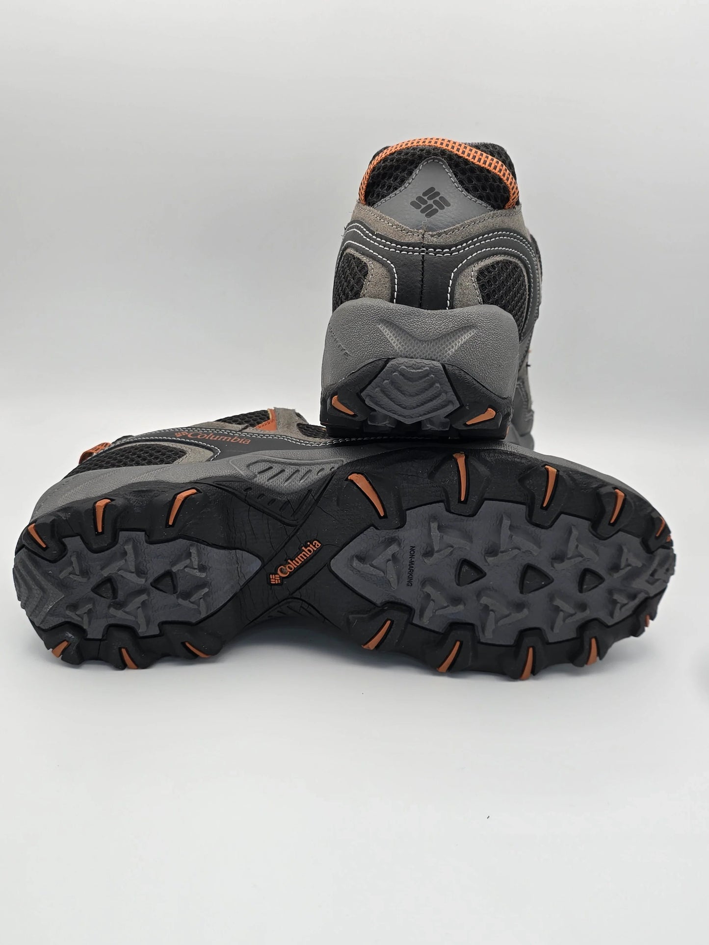 Graue Outdoor-Schuhe mit orangefarbenen Details und robuster Profilsohle auf weißem Hintergrund