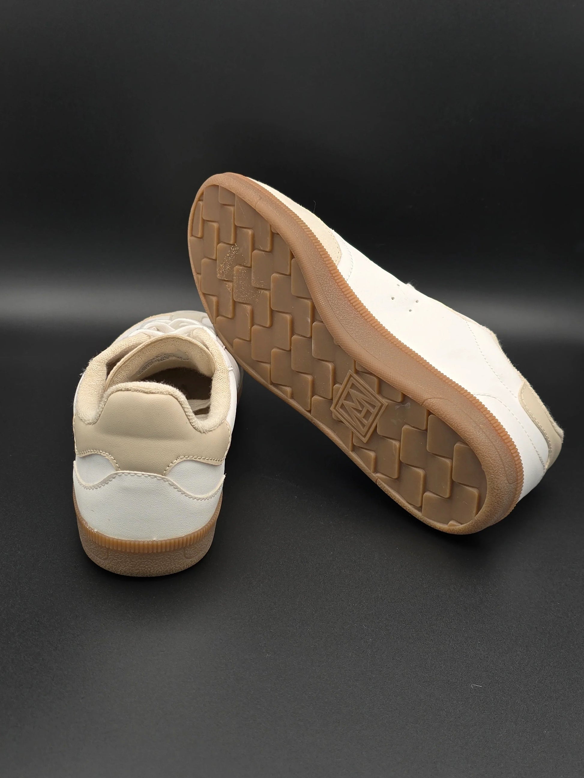 Beige und weiße Sneaker mit brauner Gummisohle auf schwarzem Hintergrund, modische Schuhe