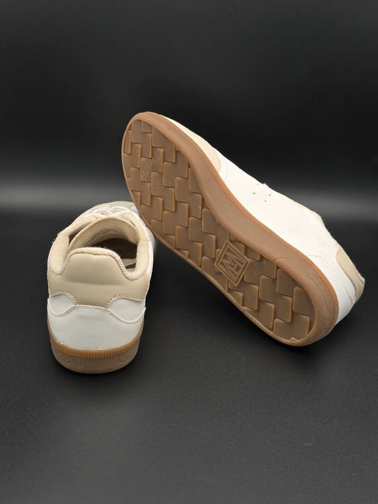 Beige und weiße Sneaker mit brauner Gummisohle auf schwarzem Hintergrund, modische Schuhe