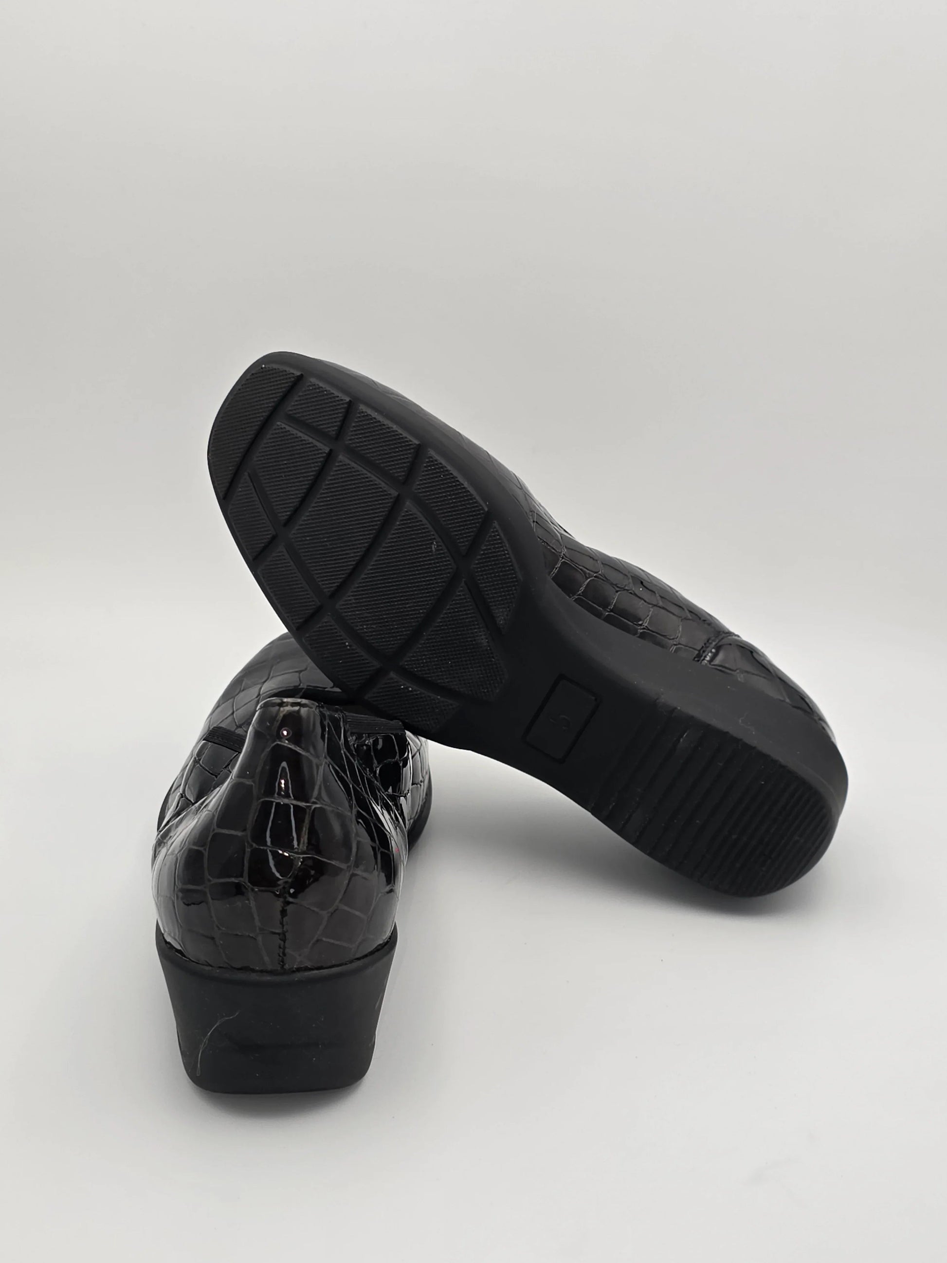 Schwarze Damenschuhe mit Kroko-Prägung und rutschfester Sohle auf weißem Hintergrund