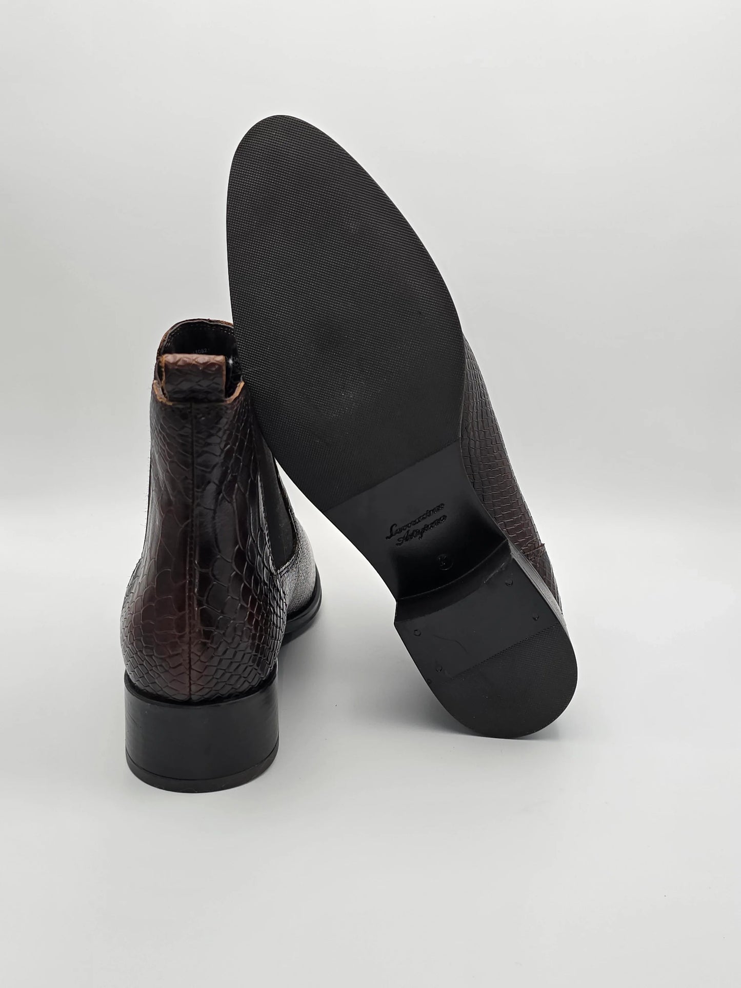 Elegante Herrenstiefel mit brauner Schlangenleder-Optik und Gummisohle auf weißem Hintergrund