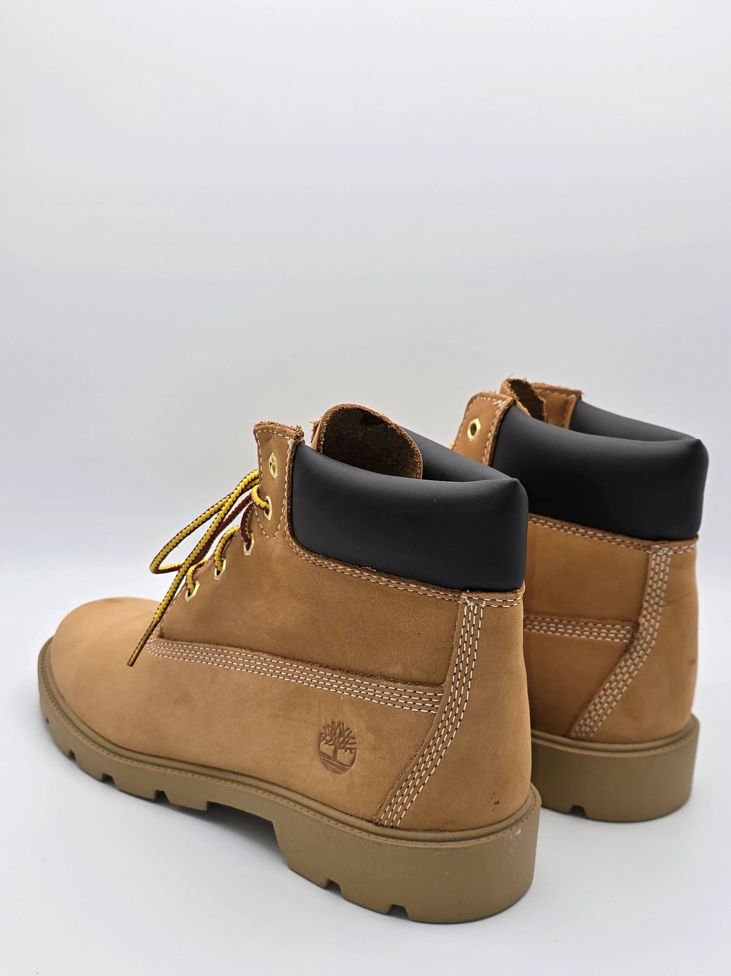 Zwei braune Nubukleder-Boots mit schwarzem Schaft und gelben Schnürsenkeln auf weißem Hintergrund