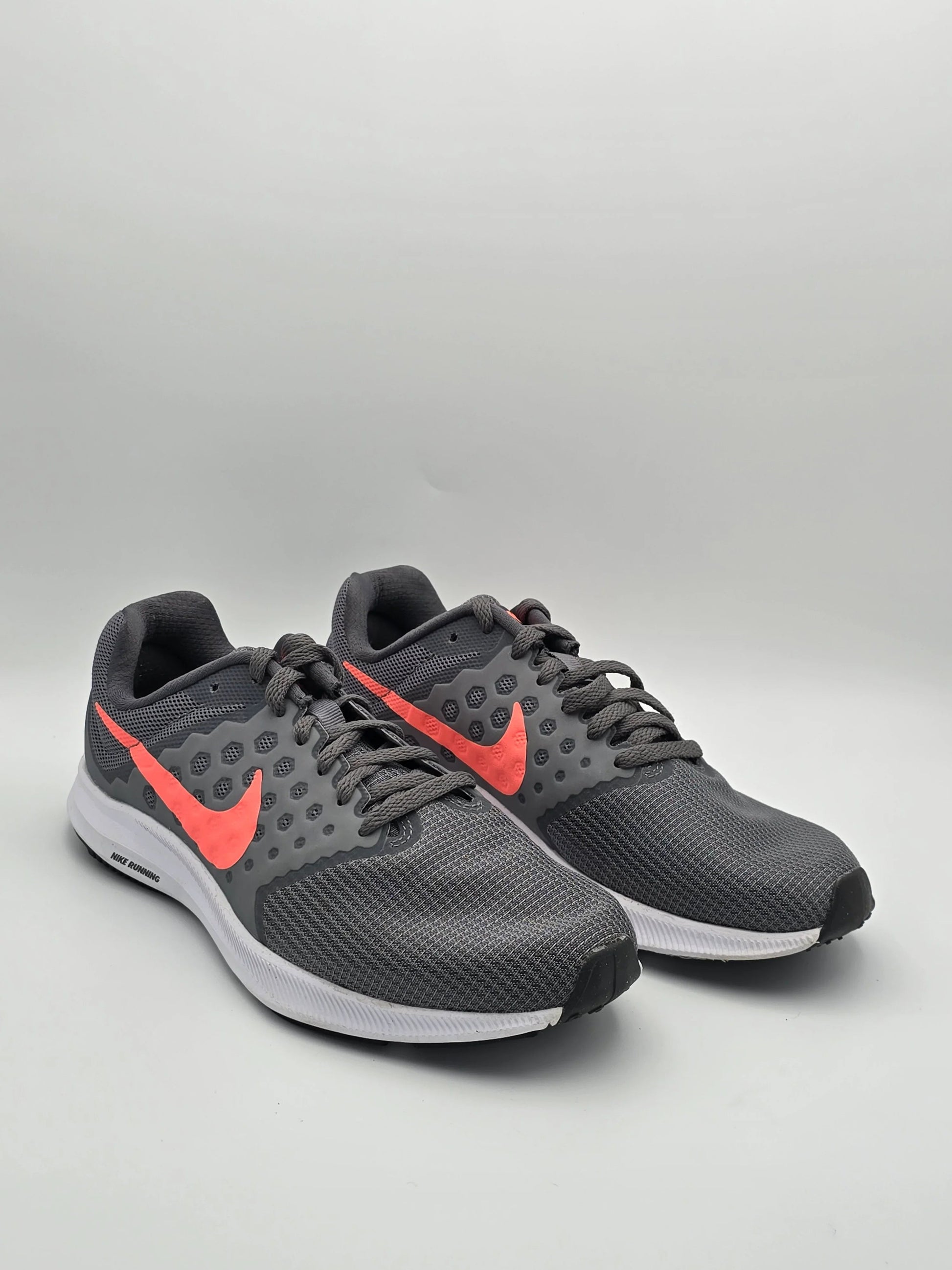 Graue Sportschuhe mit Netzstruktur, leuchtend rotem Logo und weißer Sohle auf neutralem Hintergrund