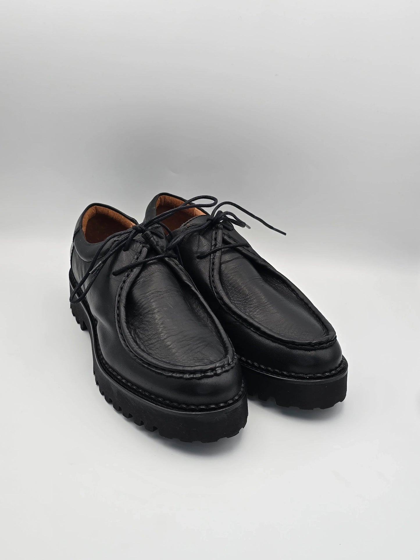 Schwarze Lederschuhe mit Profilsohle und Schnürsenkeln auf weißem Hintergrund