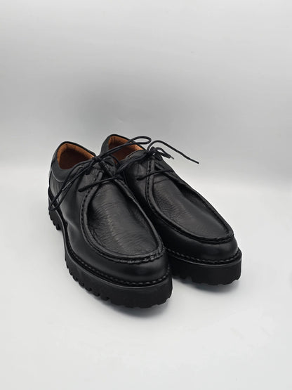 Schwarze Lederschuhe mit Profilsohle und Schnürsenkeln auf weißem Hintergrund