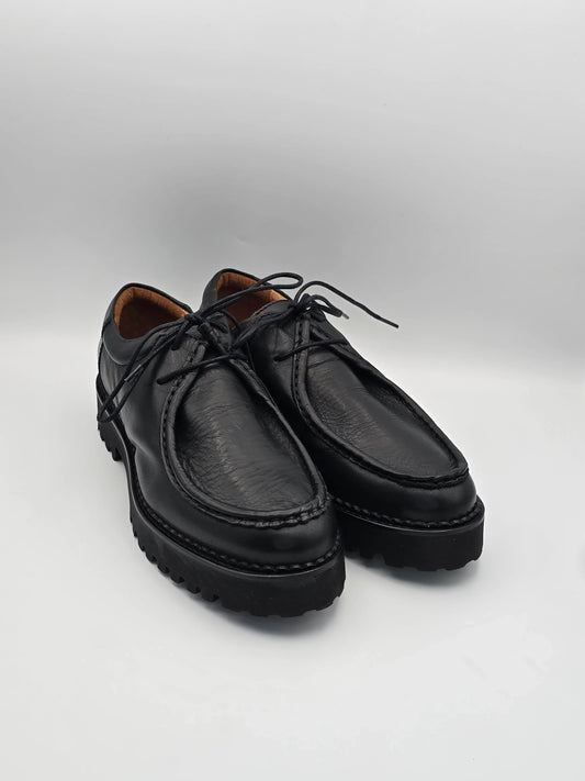 Schwarze Lederschuhe mit Profilsohle und Schnürsenkeln auf weißem Hintergrund