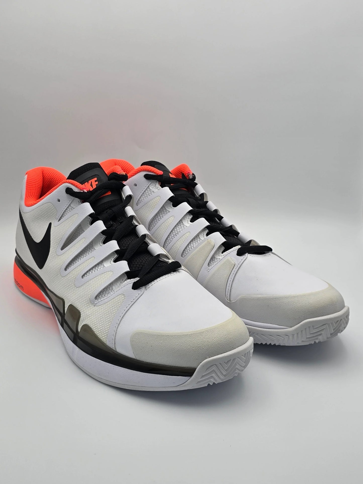 Weiße Sneaker mit schwarzem Logo, orangen Akzenten und sportlichem Design auf hellem Hintergrund.