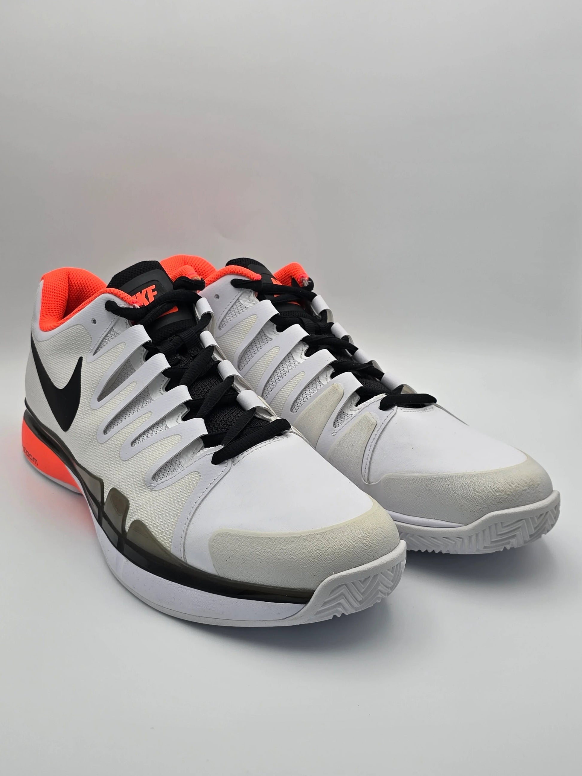 Weiße Sneaker mit schwarzem Logo, orangen Akzenten und sportlichem Design auf hellem Hintergrund.