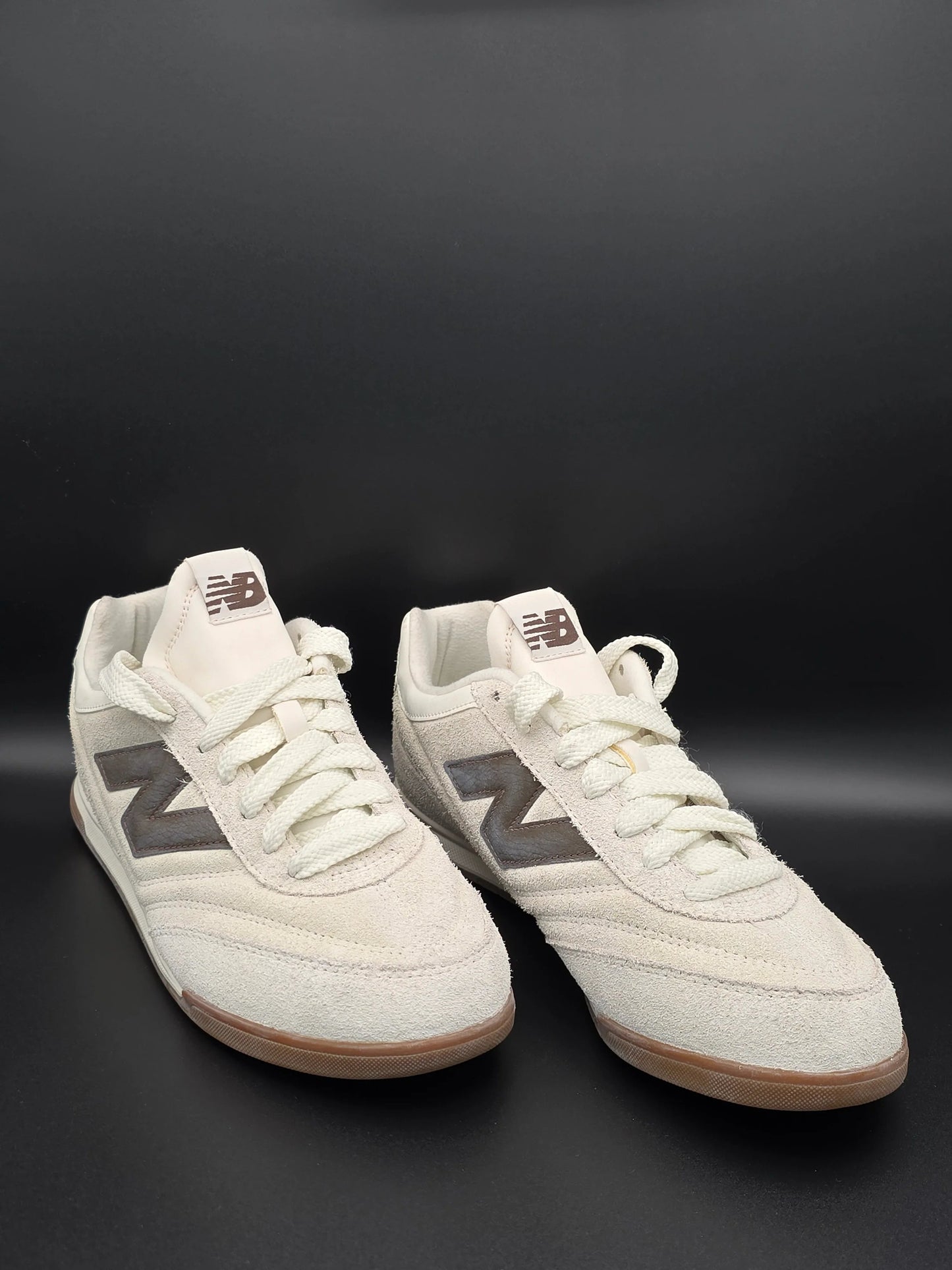 Beige Sneaker aus Wildleder mit braunem Logo, nachhaltige Mode vor schwarzem Hintergrund
