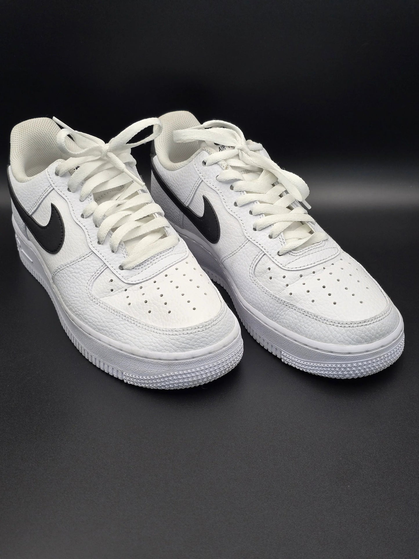 Weiße Sneaker mit schwarzem Swoosh, seitlich auf schwarzem Hintergrund fotografiert