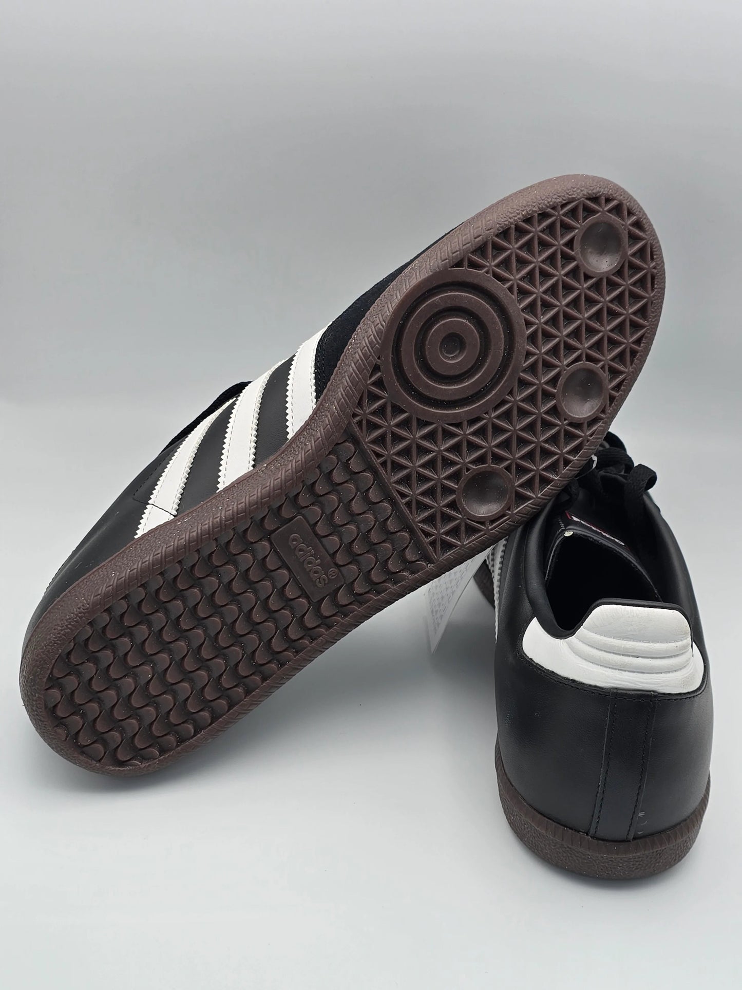 Schwarzer Sneaker mit weißen Streifen und brauner Gummisohle auf hellem Hintergrund