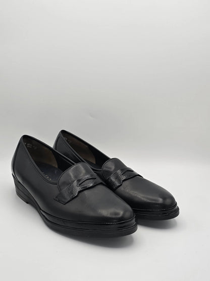 Schwarze Damen-Lederslipper mit kleiner Keilsohle und Zierspange vor weißem Hintergrund