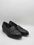 Schwarze Damen-Lederslipper mit kleiner Keilsohle und Zierspange vor weißem Hintergrund